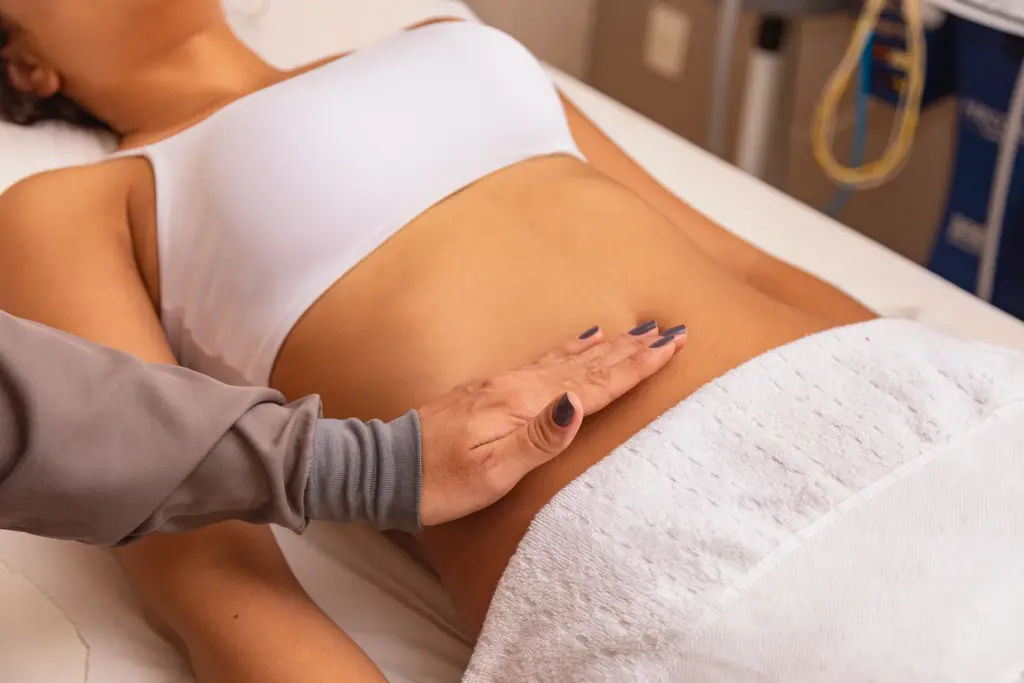 Practitioner places a hand on a woman's abdomen as she lies on a treatment table in a clinic