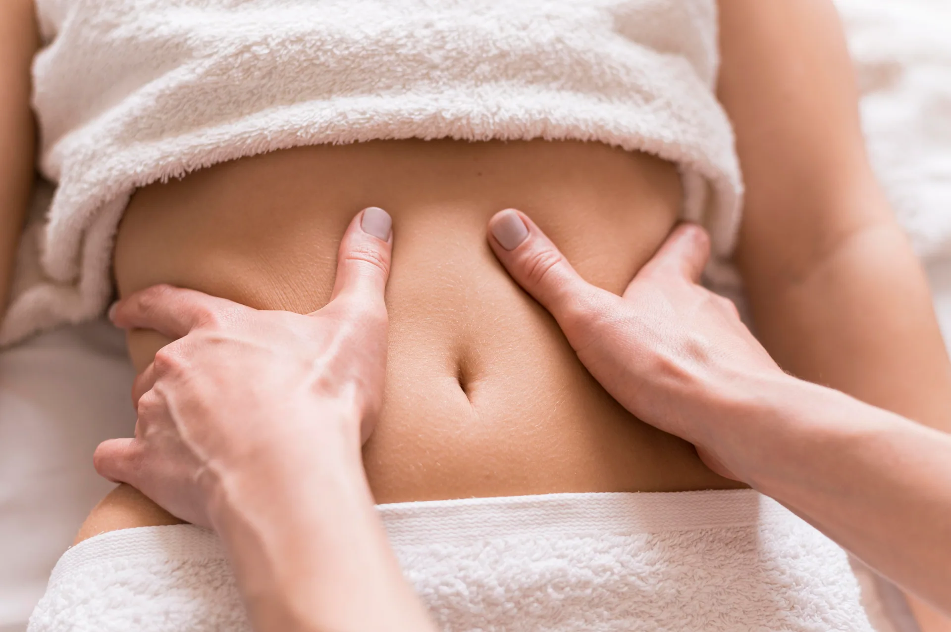 Therapist's hands performing an abdominal massage on a client draped in white towels.