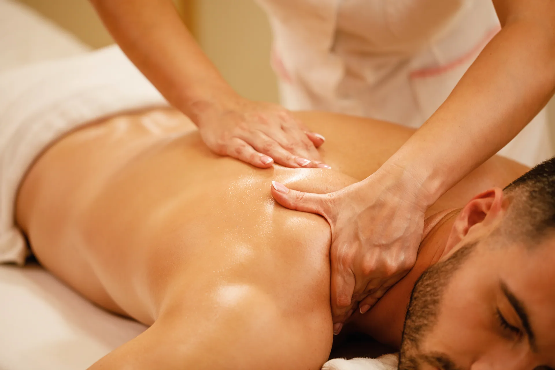 Massage therapist uses both hands to work the upper back and shoulder of a man lying face down on a massage table.