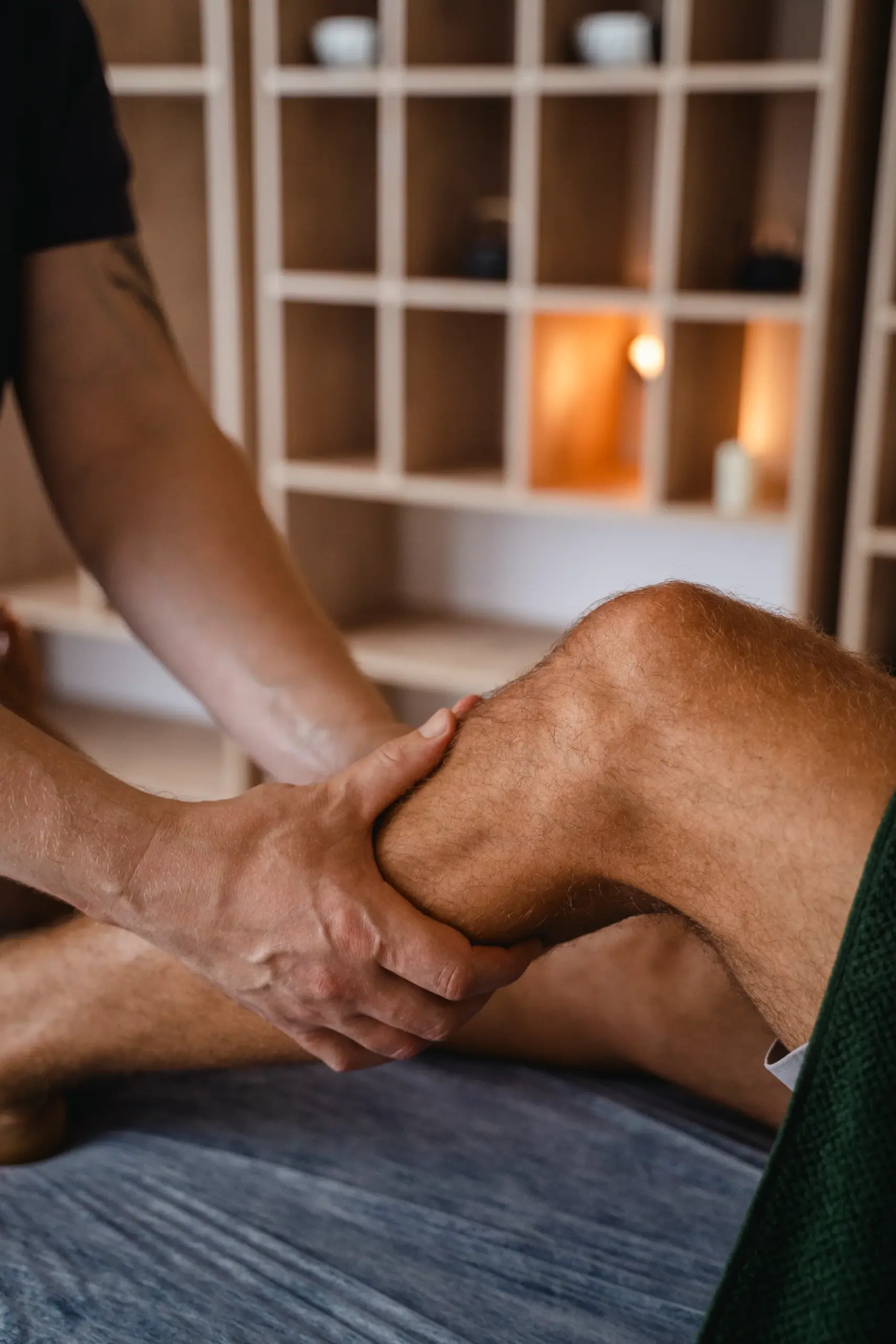 Massage therapist using both hands to work on a client's calf and knee on a massage table.
