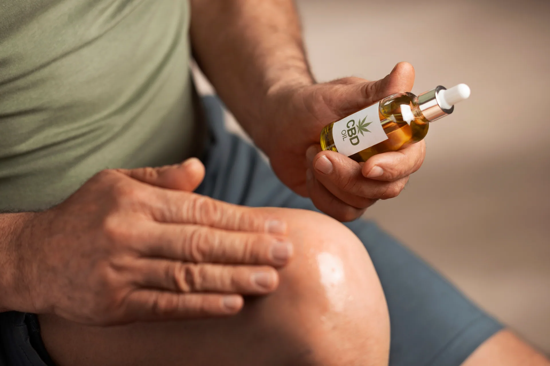 Man holding a dropper bottle of CBD oil while rubbing oil onto his knee