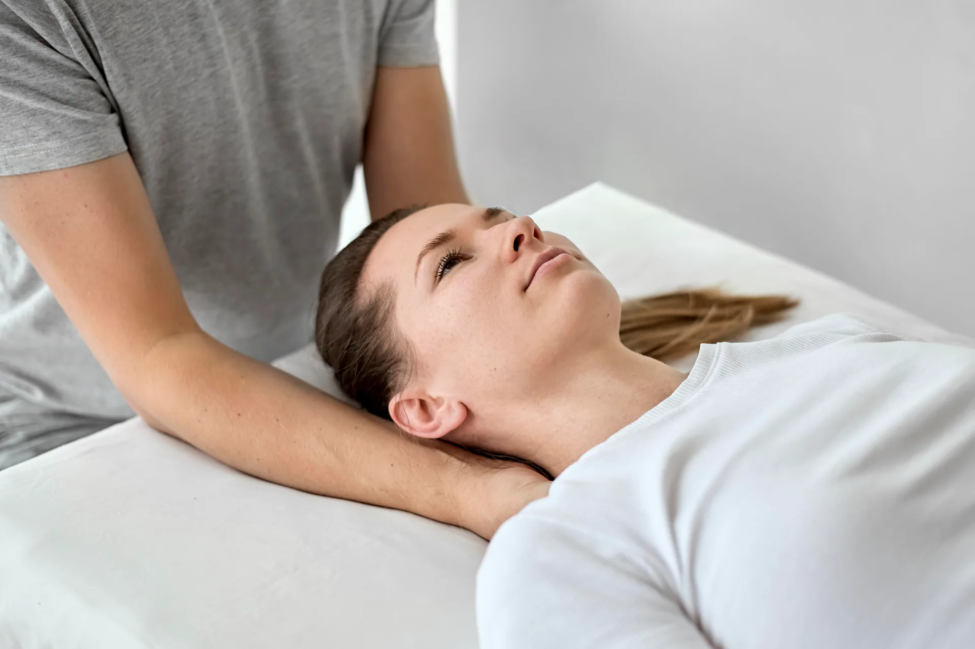 Practitioner cradles the neck of a woman lying face up on a white treatment table during a chiropractic session.