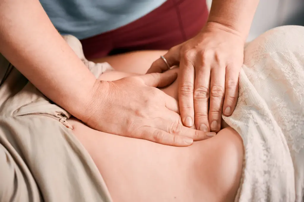 Therapist's hands pressing gently on a client's abdomen during a massage therapy session.