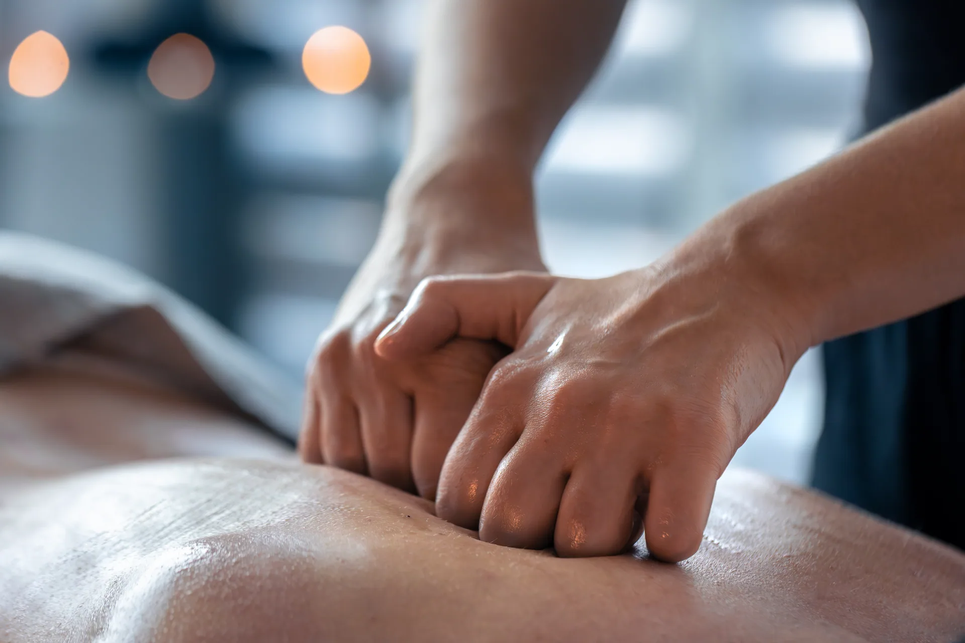 Close-up of a massage therapist's hands applying knuckle pressure to a client's back during a deep tissue massage.