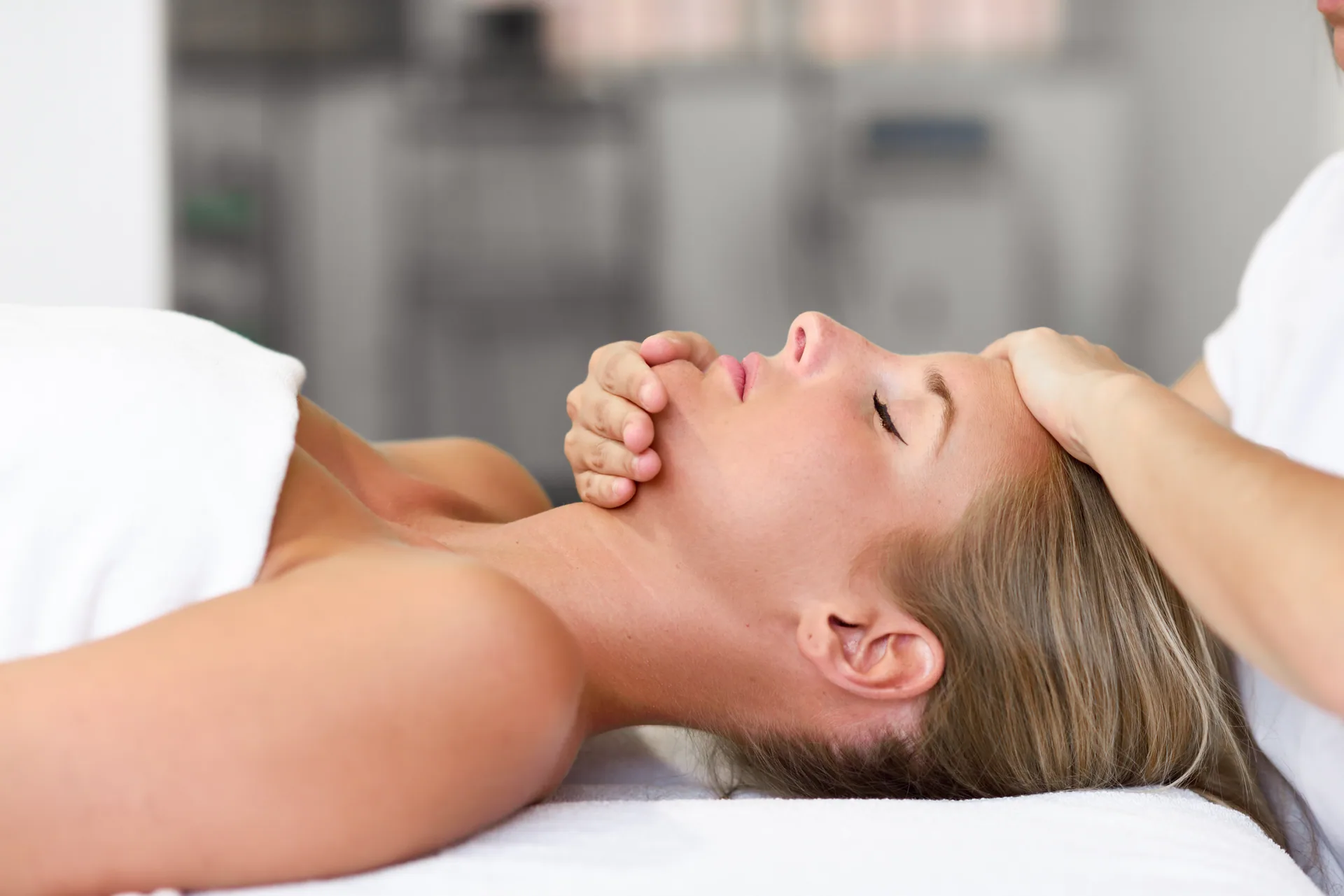 Woman lying on a massage table receiving a facial and scalp massage from a therapist's hands.