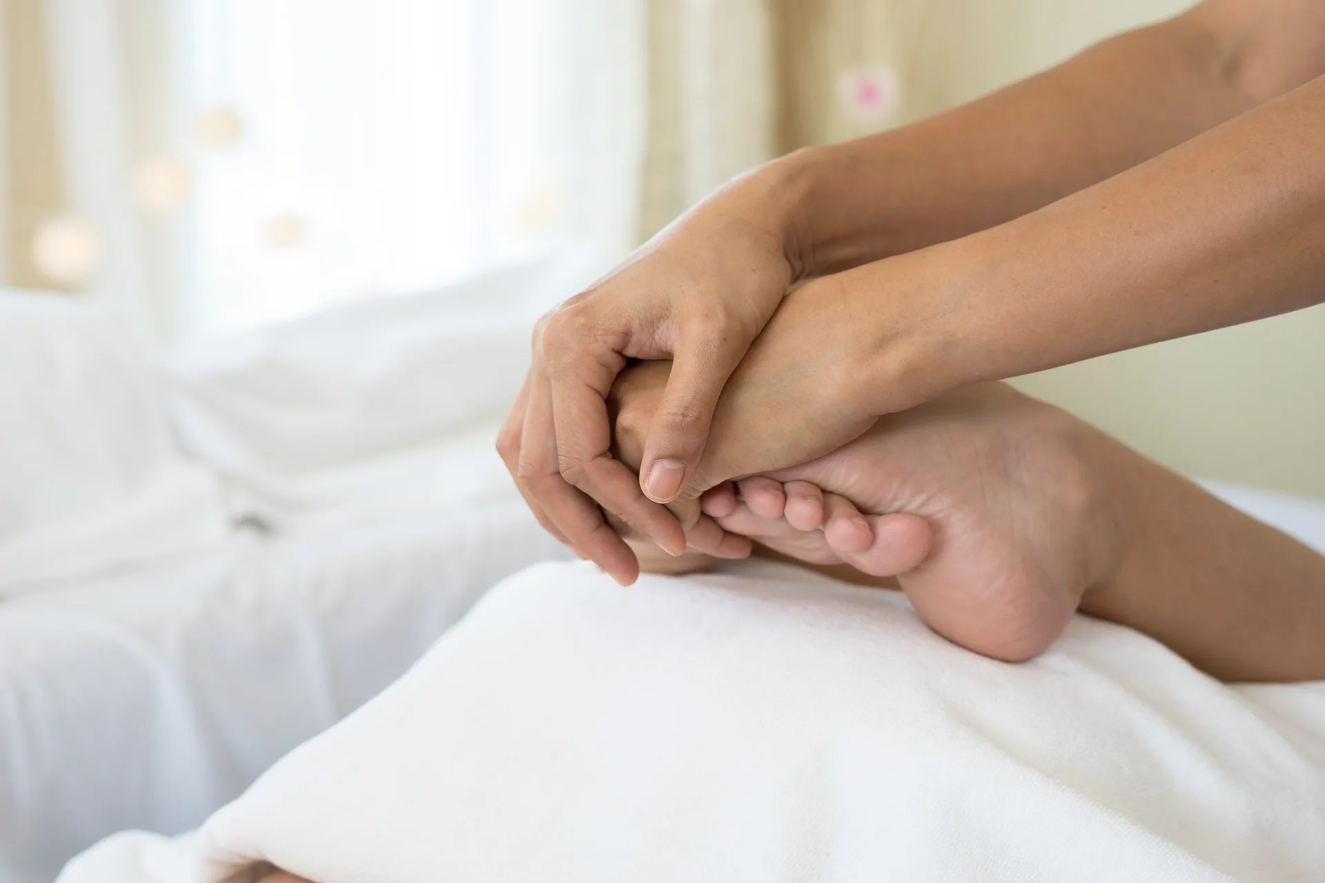 Close-up of a therapist's hands massaging a client's foot on a white massage table.