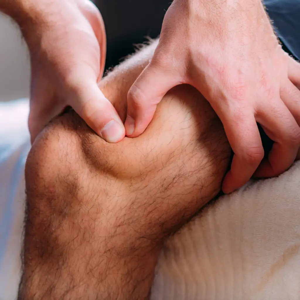 Therapist's hands pressing into the area above a man's knee during a massage treatment