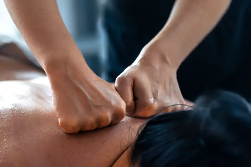Massage therapist pressing both fists into a client's bare upper back during a deep tissue session