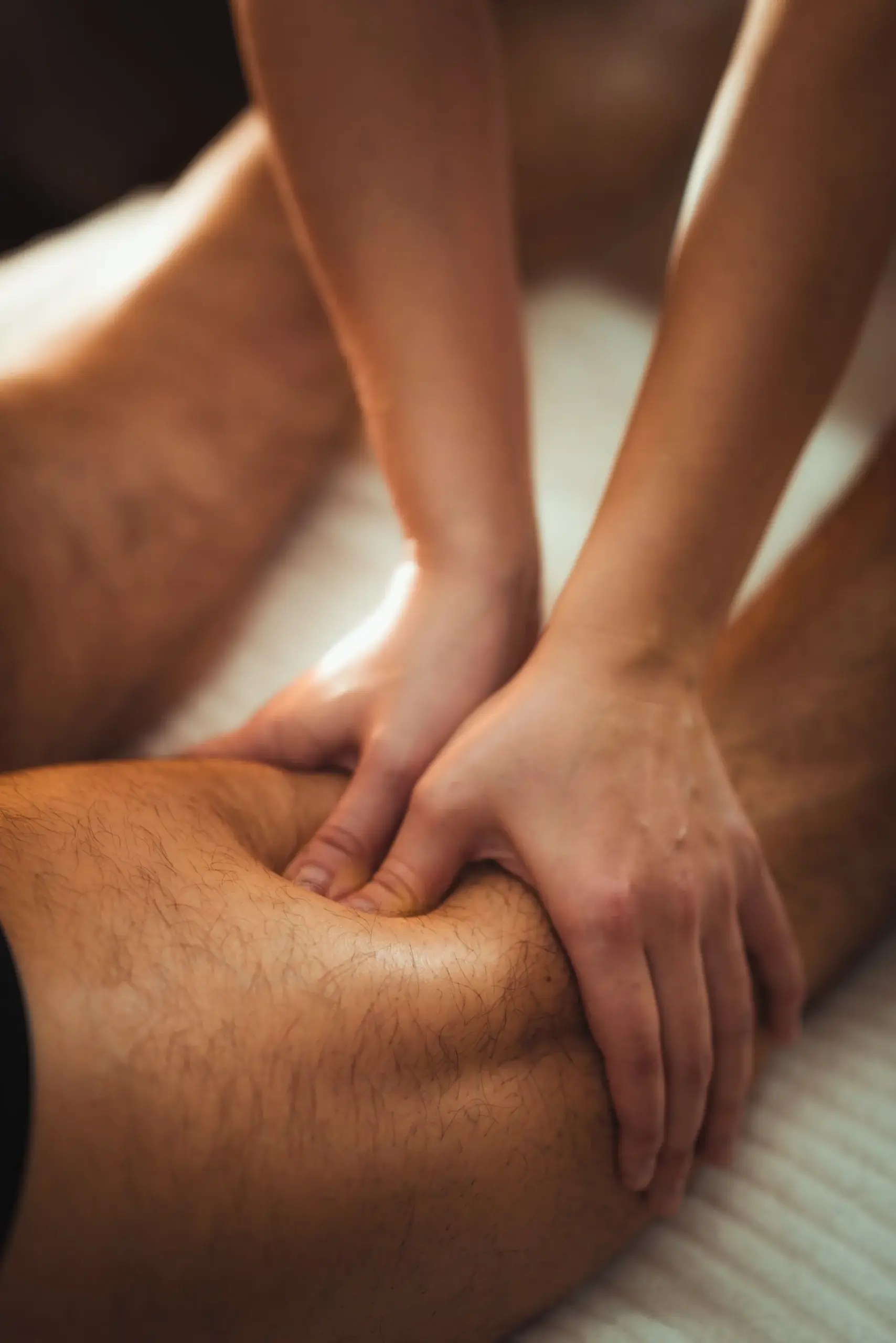 Massage therapist's hands pressing into a client's thigh during a deep tissue massage session.