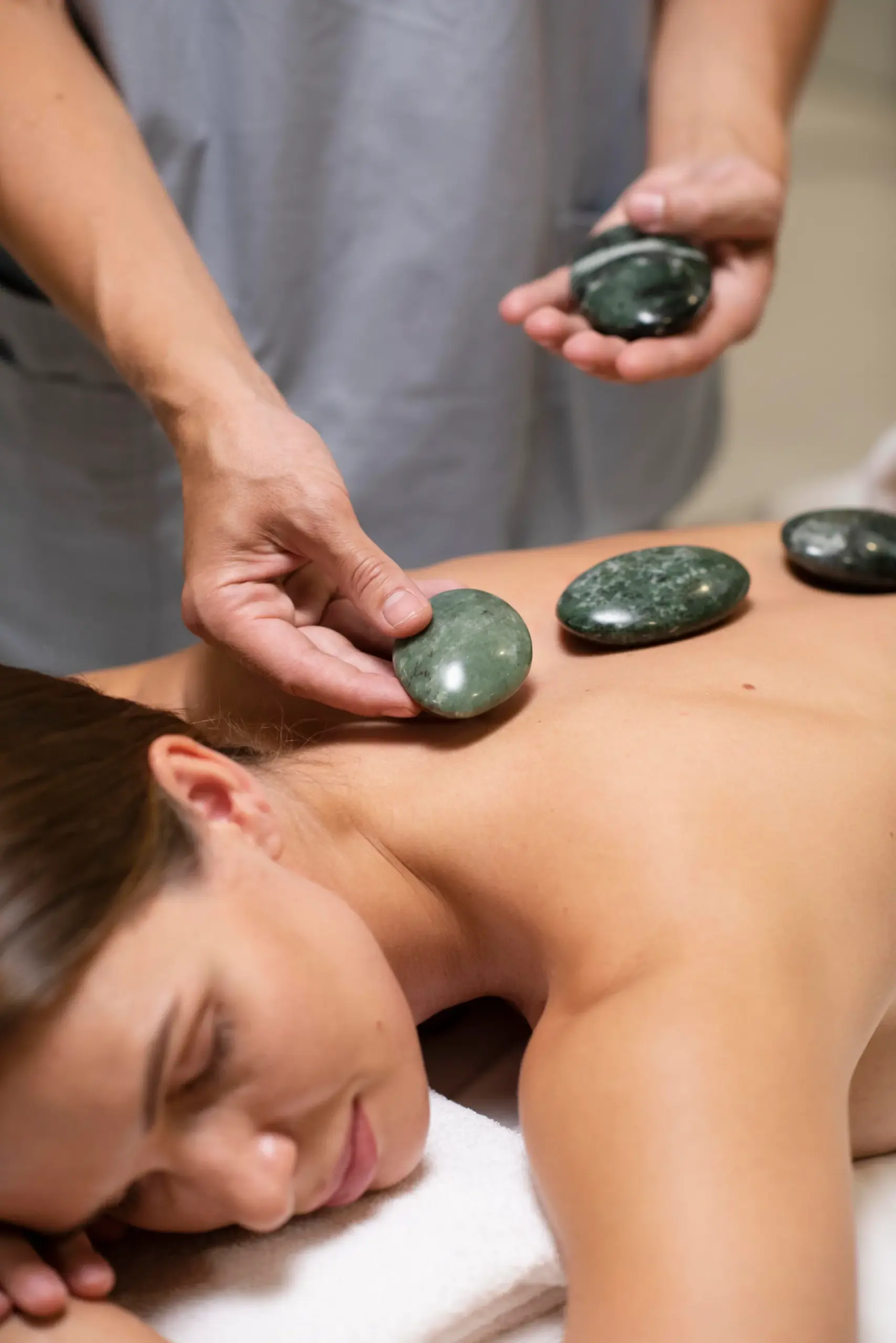 Massage therapist placing smooth green stones along a woman's back during a hot stone massage