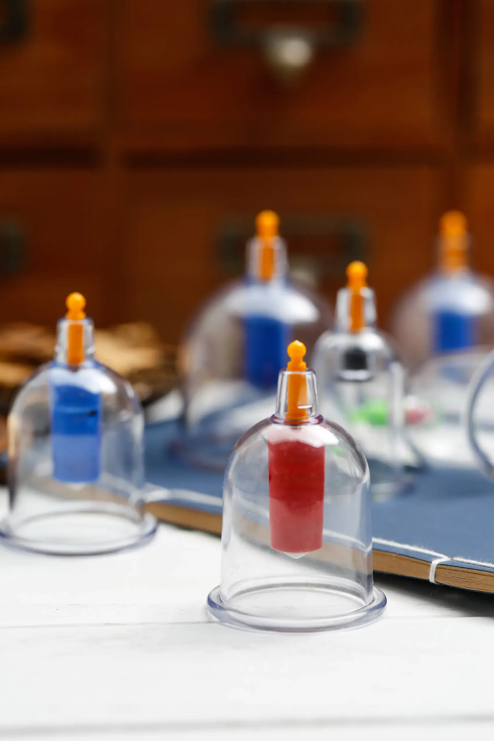 Clear plastic vacuum cupping cups with orange valves arranged on a white table in front of a wooden cabinet.