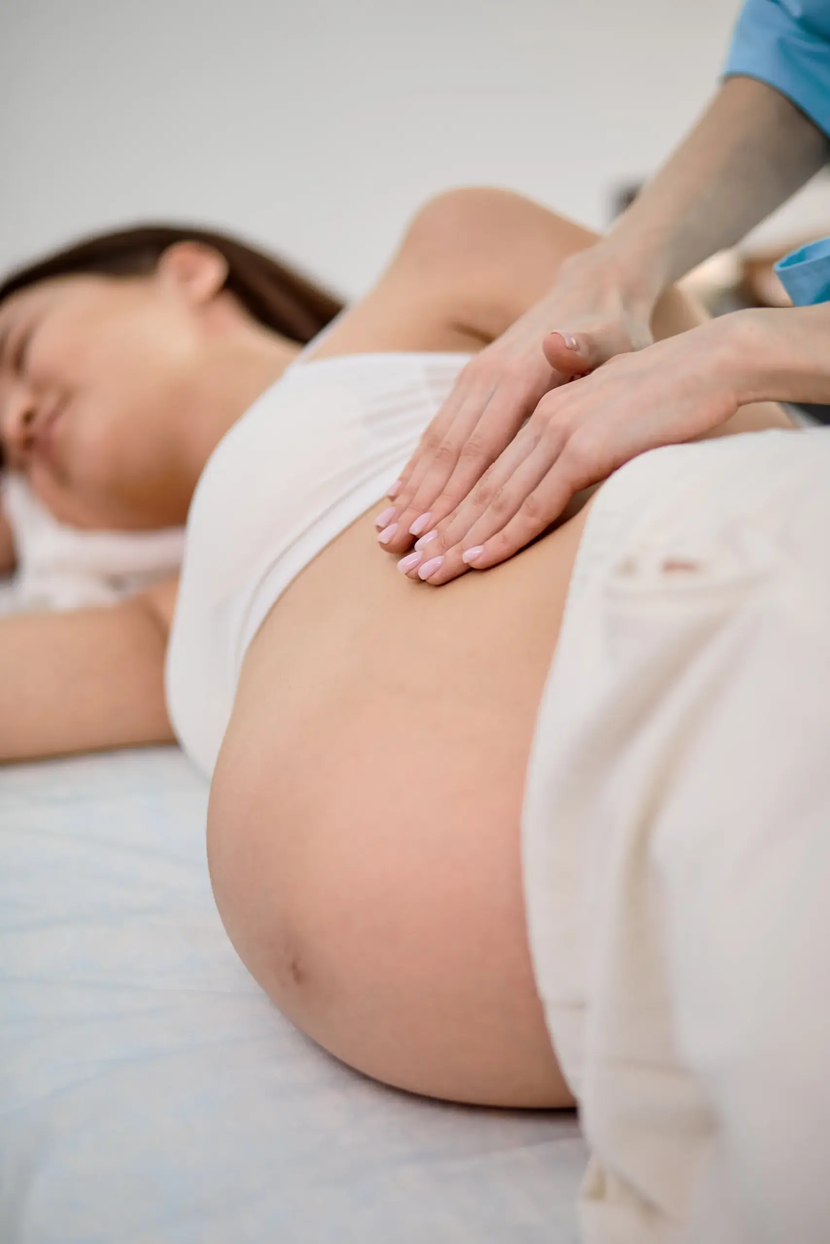 Pregnant woman lying on her side while a massage therapist places hands on her upper abdomen