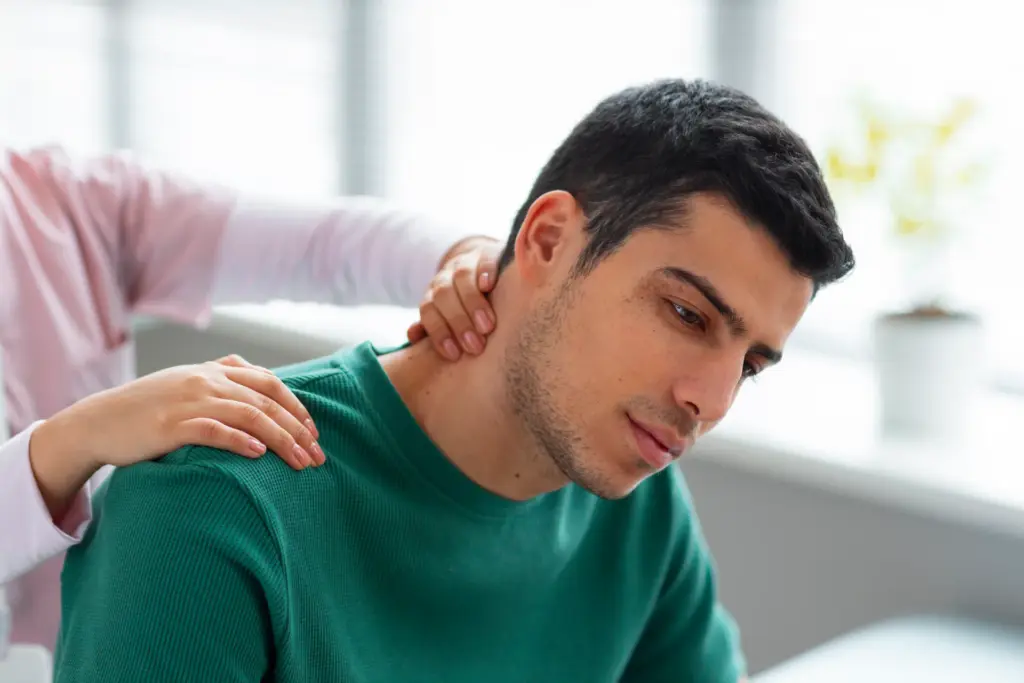 Massage therapist's hands working on the neck and shoulder of a seated man in a green shirt