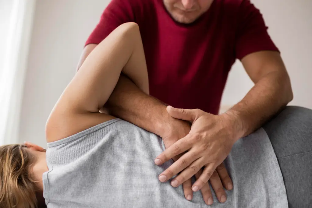 Massage therapist pressing both hands into the lower back of a woman lying on her side on a treatment table.